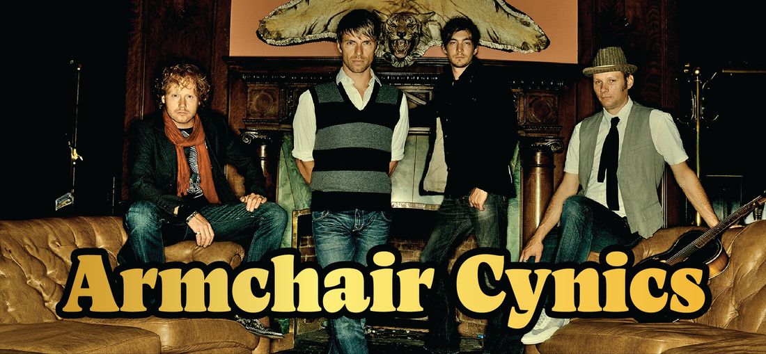 	 Four men stand and sit in a vintage-style room with brown leather sofas and a fireplace. A large taxidermy animal head is mounted above the mantle. Bold yellow text reads Armchair Cynics.